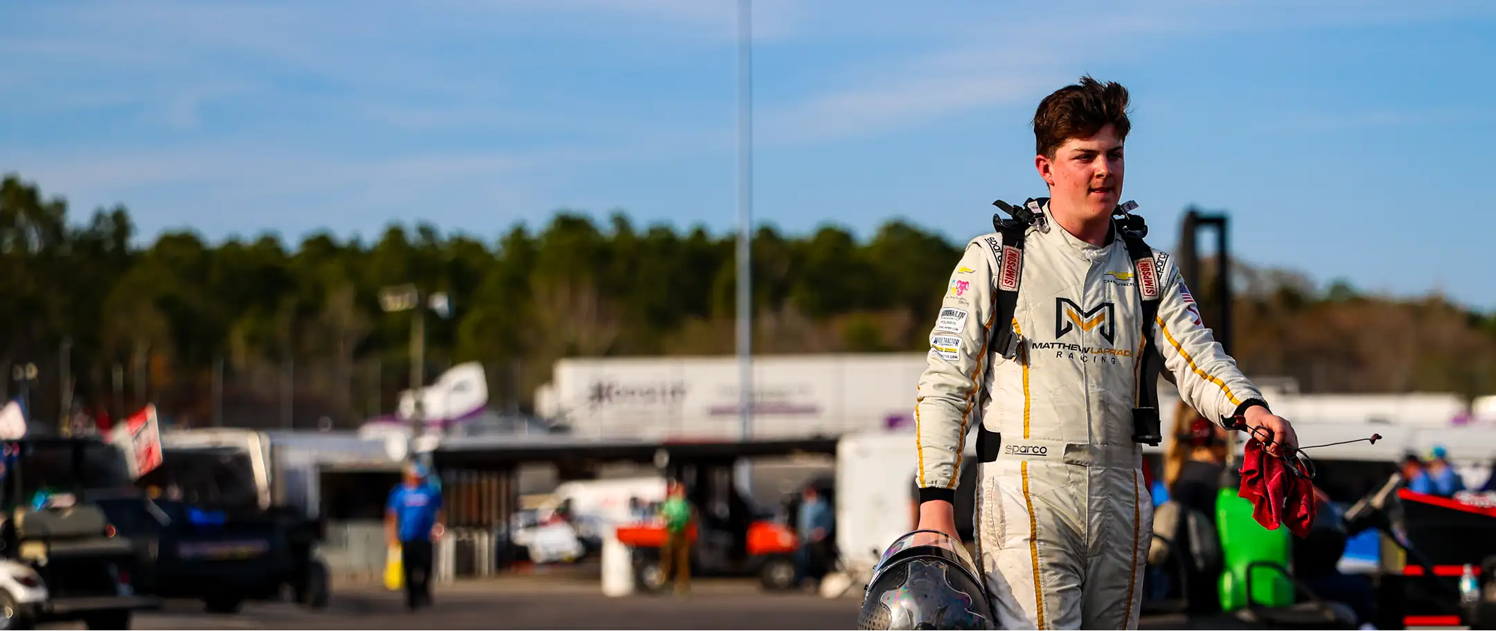Matthew Laprade walking through the pits in his racing suit, helmet in hand